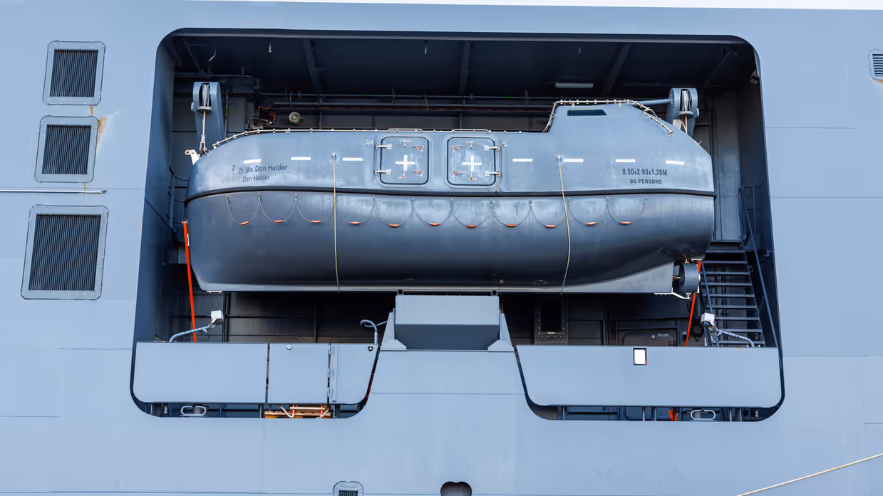 Een grijze kraan op het dek van het schip, een donkergrijze reddingsboot en het predicaat met daarop ‘Den Helder’.