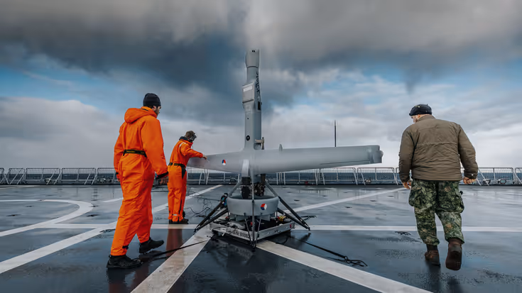 V-Bat op een dek van een marineschip met drie medewerkers.