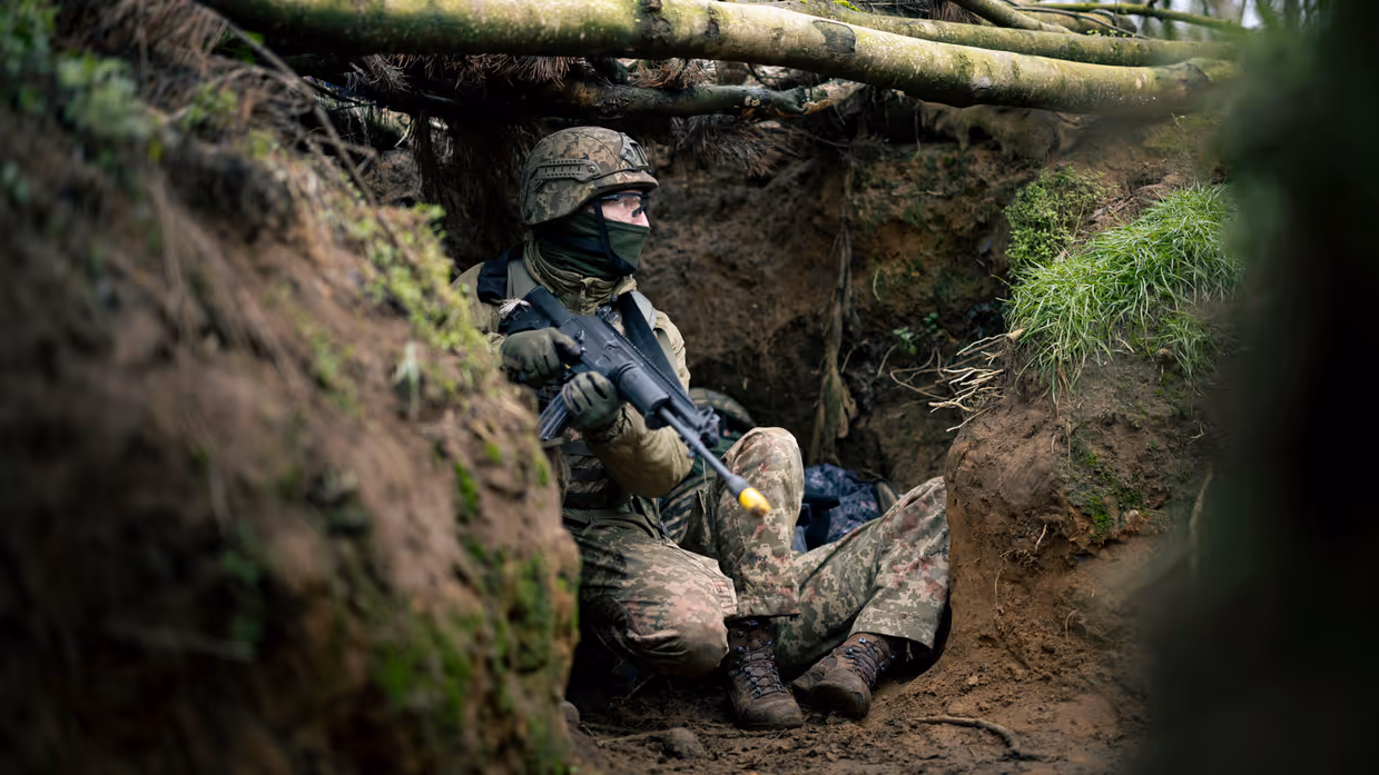 Een Oekraïense militair met een geweer in zijn hand, kijkt gespannen naar buiten vanuit een loopgraaf.