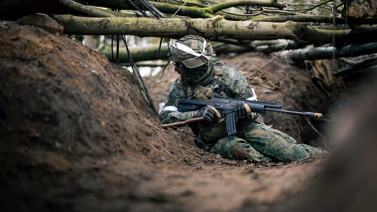 Een militair zit op zijn heupen in een loopgraaf. 