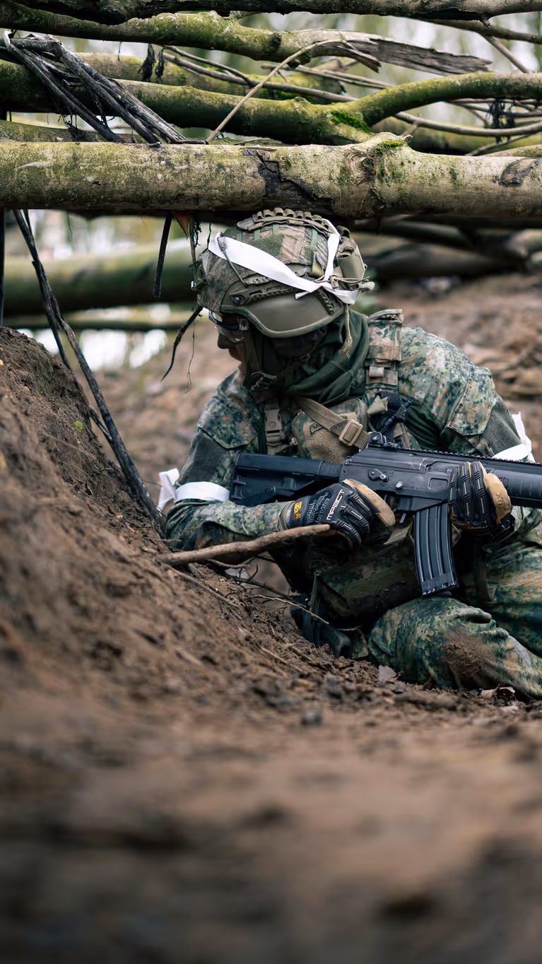 Een militair zit op zijn heupen in een loopgraaf. 