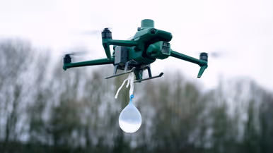 Een drone hangt laag in de lucht met een waterballon eronder.