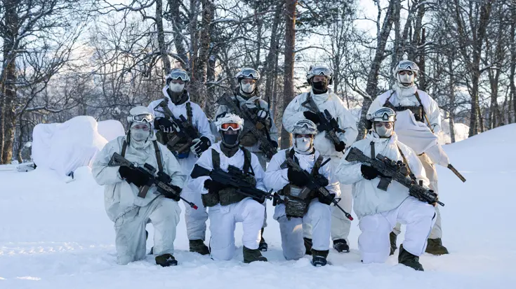 Groepsfoto van 8 gewapende mariniers in wit camo.