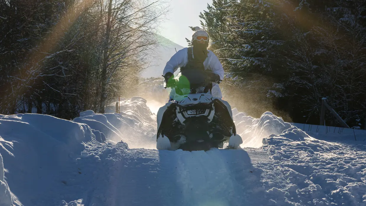 Foto links: een marinier rijdt met zijn sneeuwscooter tussen bosschages door. Foto rechts: een marinier komt met zijn sneeuwscooter los van de grond.