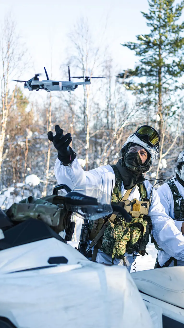 Korporaal Dani en marinier 1 Giovanni met hun sneeuwscooters in de natuur. Dani laat een drone op.