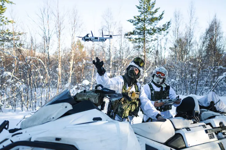 Korporaal Dani en marinier 1 Giovanni met hun sneeuwscooters in de natuur. Dani laat een drone op.