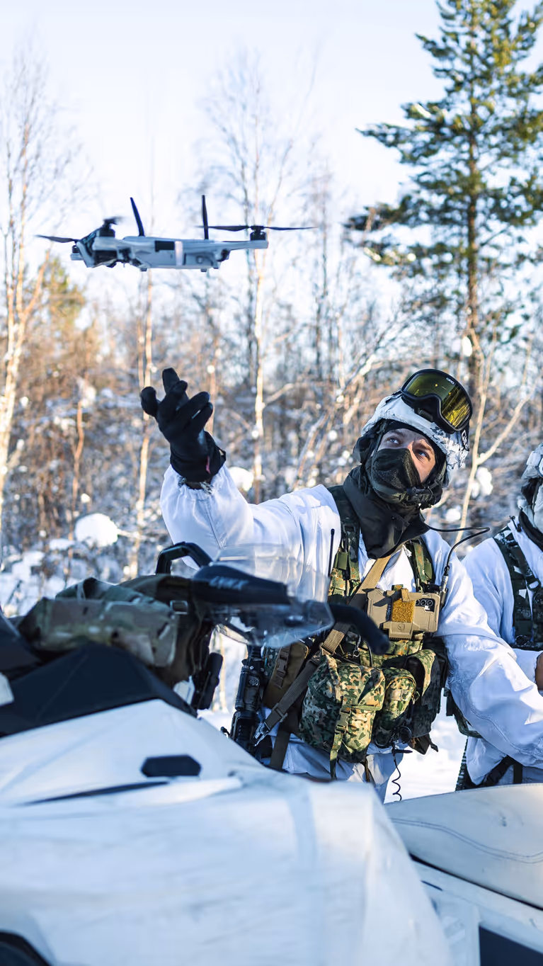 Korporaal Dani en marinier 1 Giovanni met hun sneeuwscooters in de natuur. Dani laat een drone op.