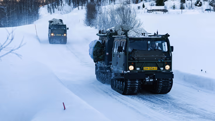 Twee rupsvoertuigen van het type BV 206 rijden over een besneeuwde weg.