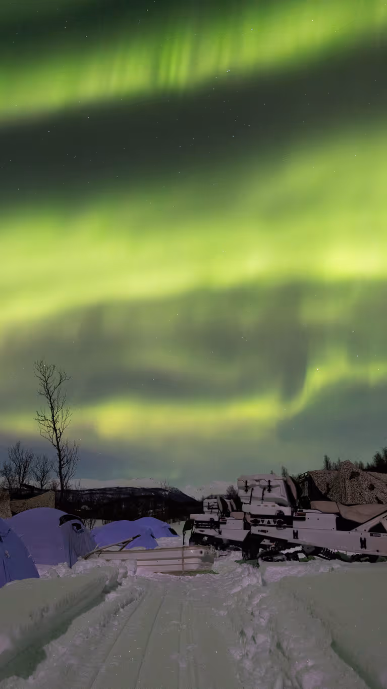 : Een tentenkamp met sneeuwscooters in een besneeuwd landschap, onder het Noorderlicht.