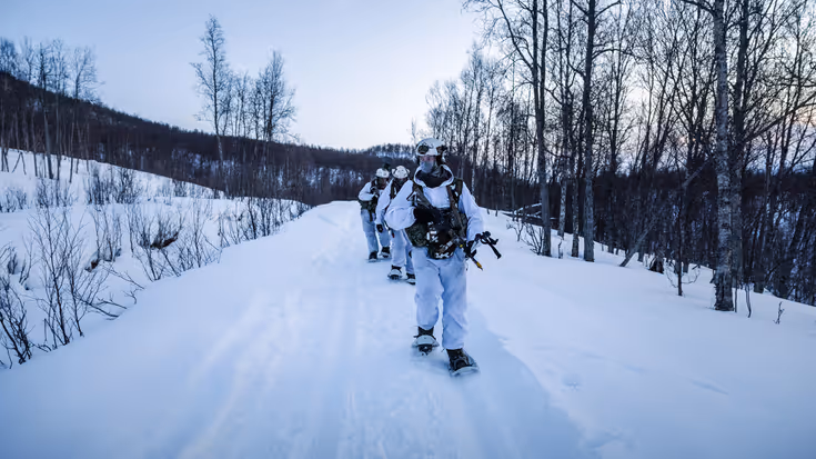 Gewapende mariniers lopen op bigfoots in ganzenpas door een besneeuwd landschap.