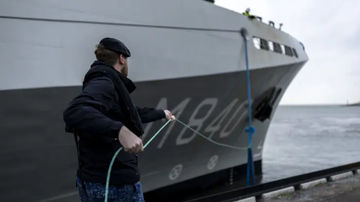 Een militair van de marine haalt met een touw een van de trossen binnen.