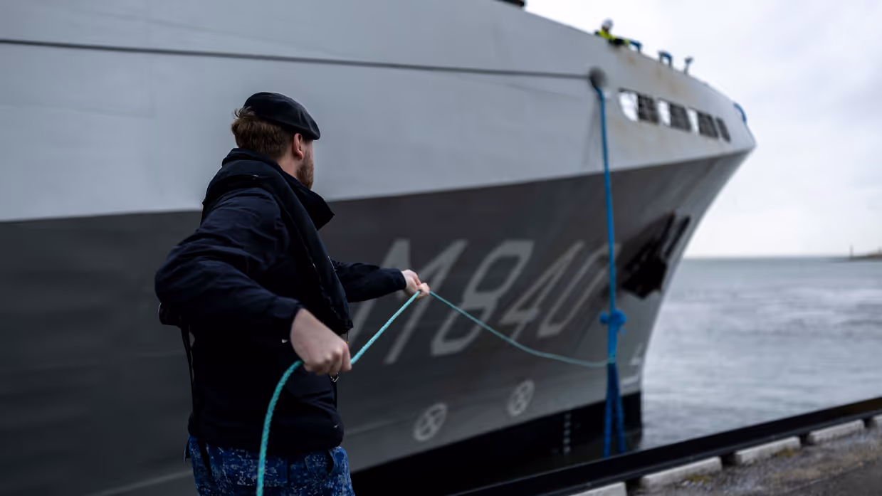 Een militair van de marine haalt met een touw een van de trossen binnen.