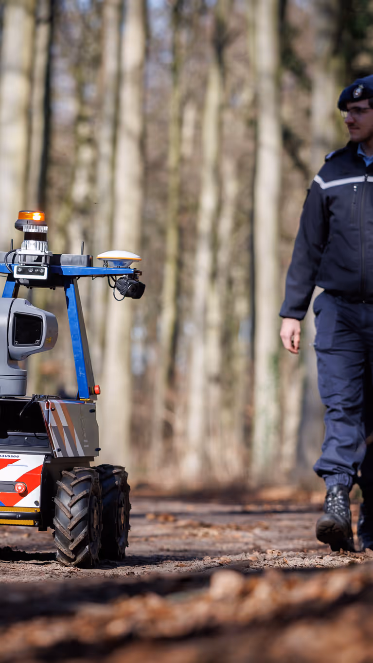 Een marechaussee loopt samen met de Roboguard door het bos.