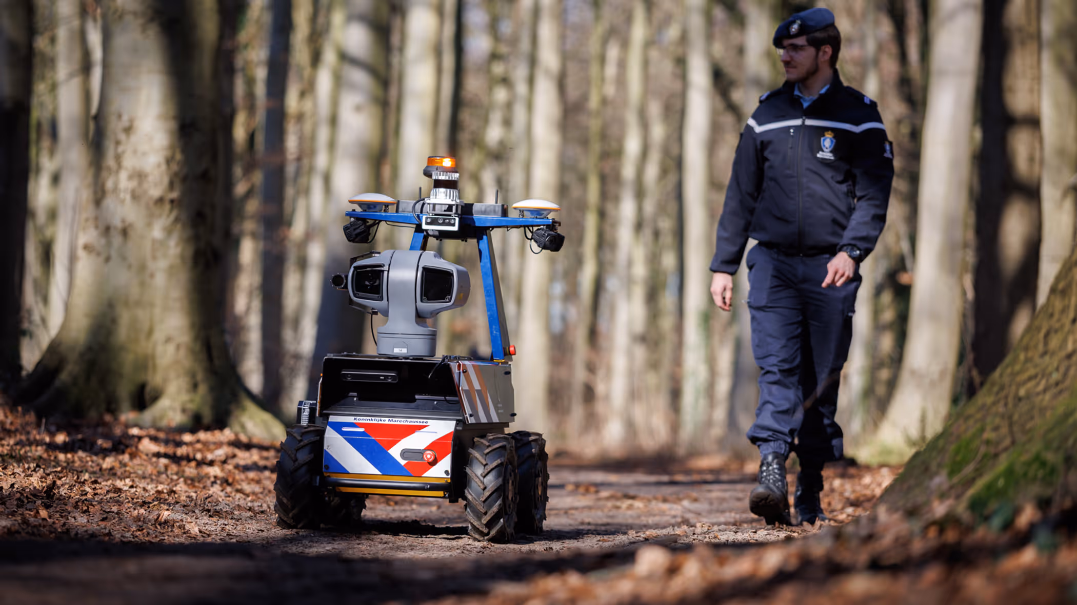 Een marechaussee loopt samen met de Roboguard door het bos.