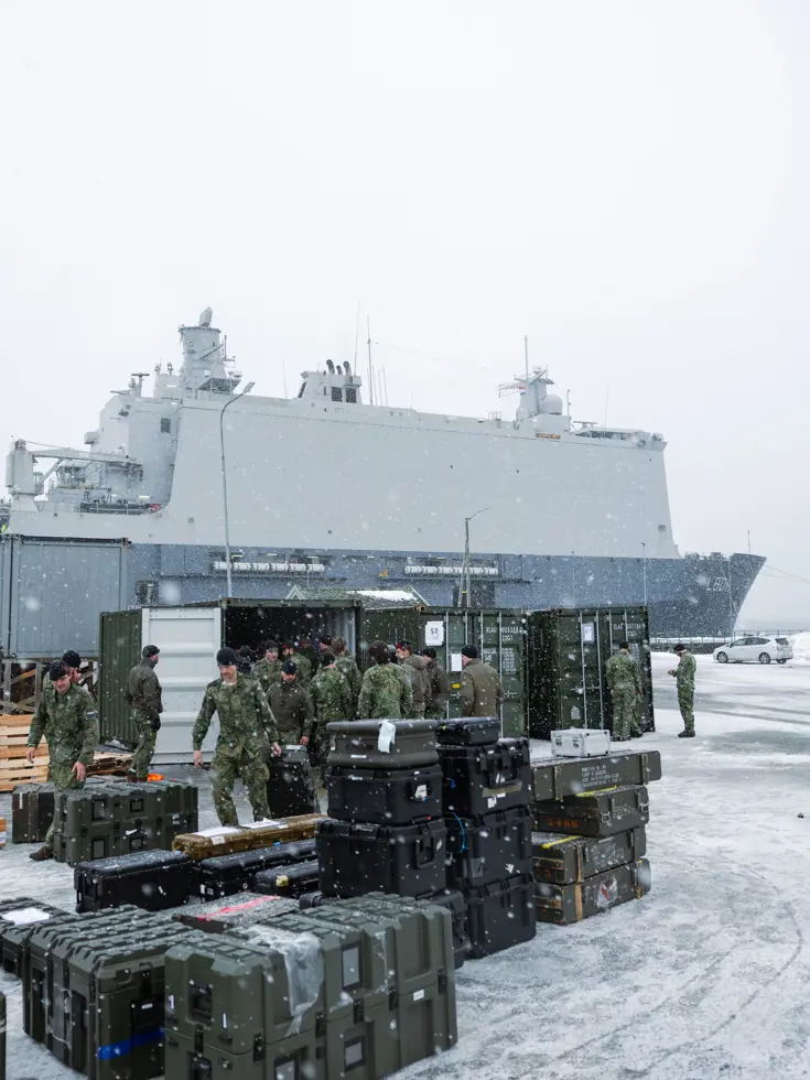 Militairen laden materieel en transportkisten uit containers in de sneeuw op de kade bij Zr.Ms. Johan de Witt. 