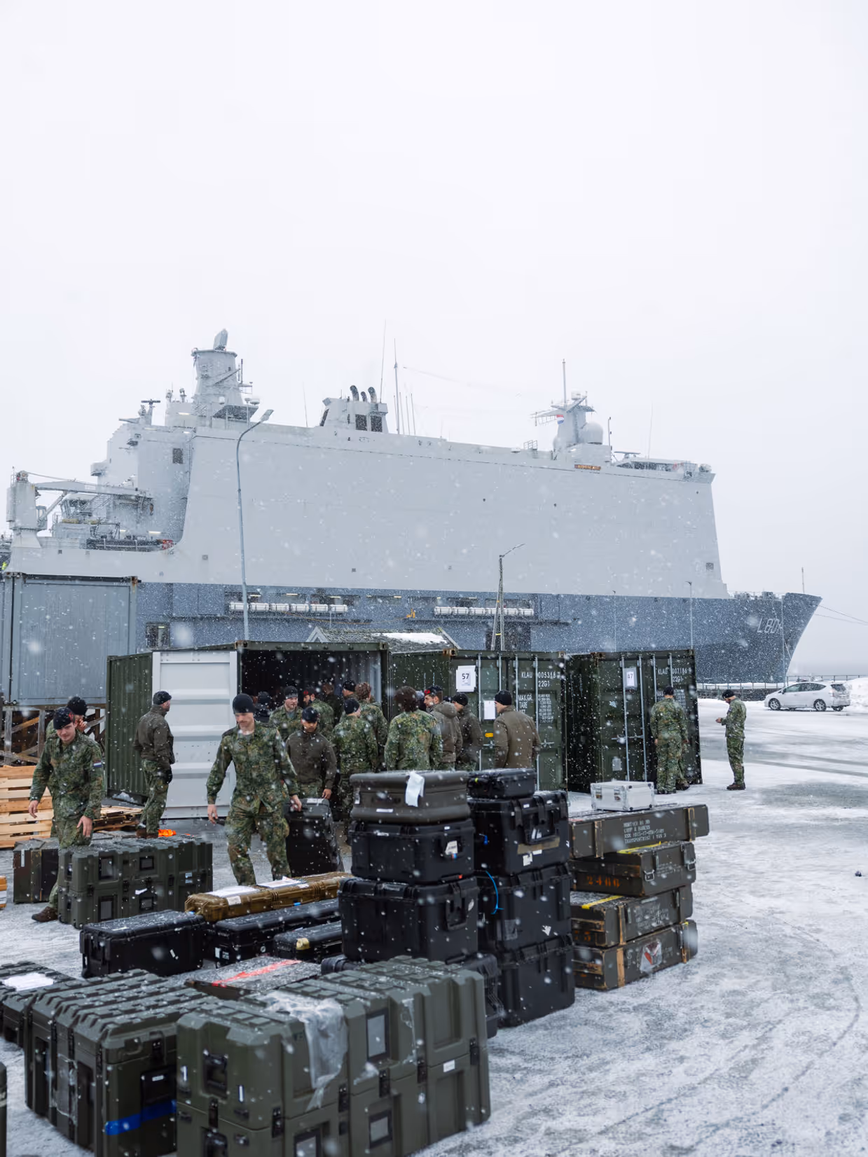 Militairen laden materieel en transportkisten uit containers in de sneeuw op de kade bij Zr.Ms. Johan de Witt. 