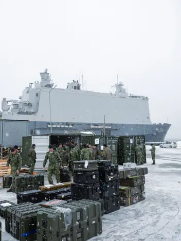 Militairen laden materieel en transportkisten uit containers in de sneeuw op de kade bij Zr.Ms. Johan de Witt. 