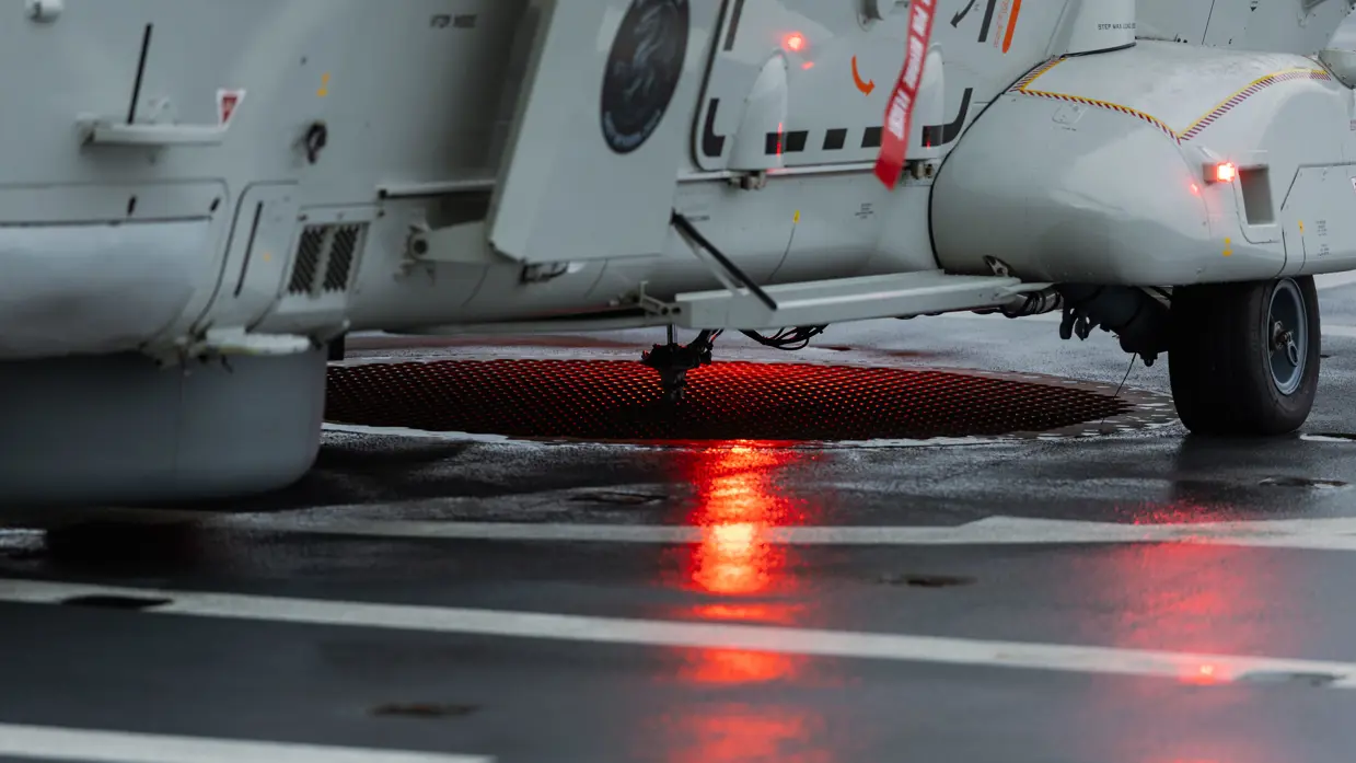 NH90-helikopter landt op het vliegdek van Zr.Ms. Johan de Witt in een Noors fjord bij schemering tijdens oefening Cold Response, terwijl dekpersoneel met lichtsignalen de landing begeleidt.