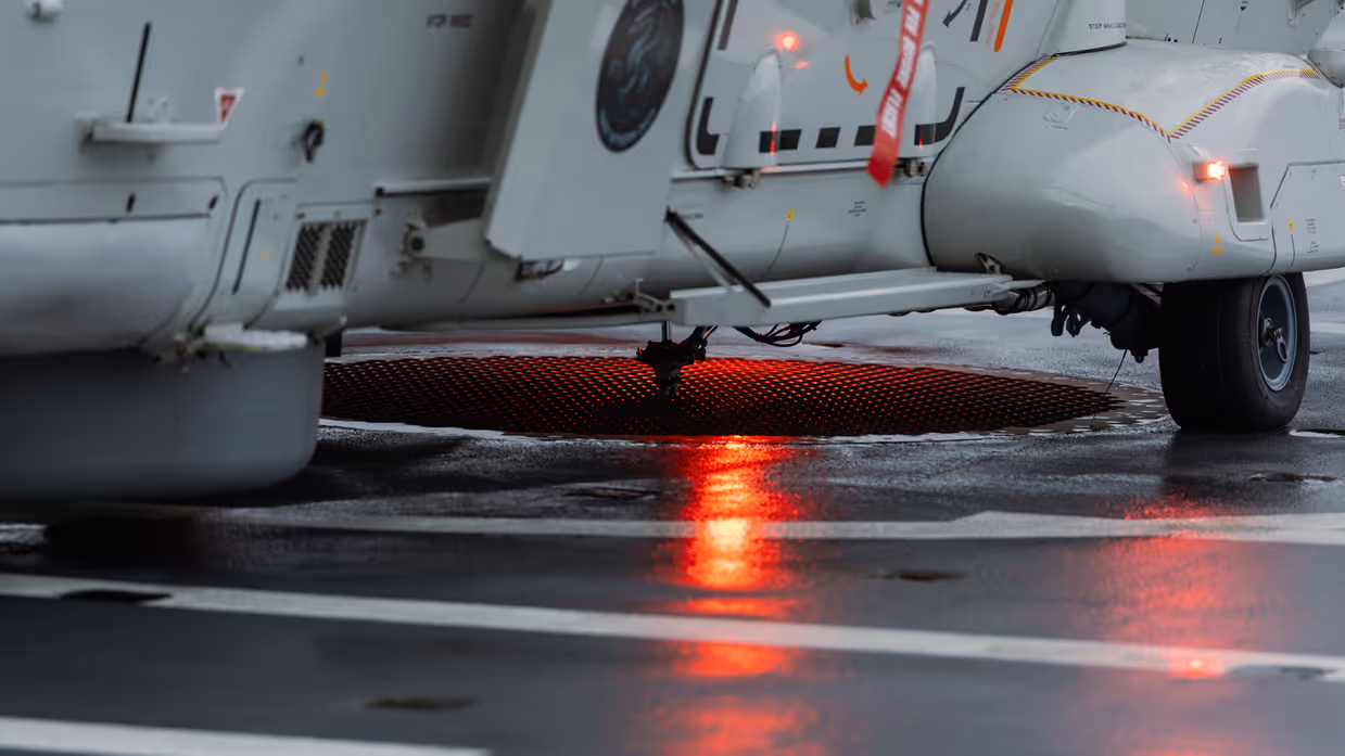 NH90-helikopter landt op het vliegdek van Zr.Ms. Johan de Witt in een Noors fjord bij schemering tijdens oefening Cold Response, terwijl dekpersoneel met lichtsignalen de landing begeleidt.