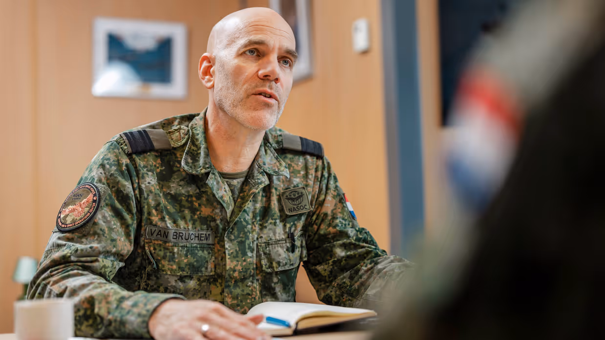Commodore Jeroen van Bruchem zit, in militair uniform, aan een tafel en praat. Daarbij maakt hij gebruik van zijn handen.