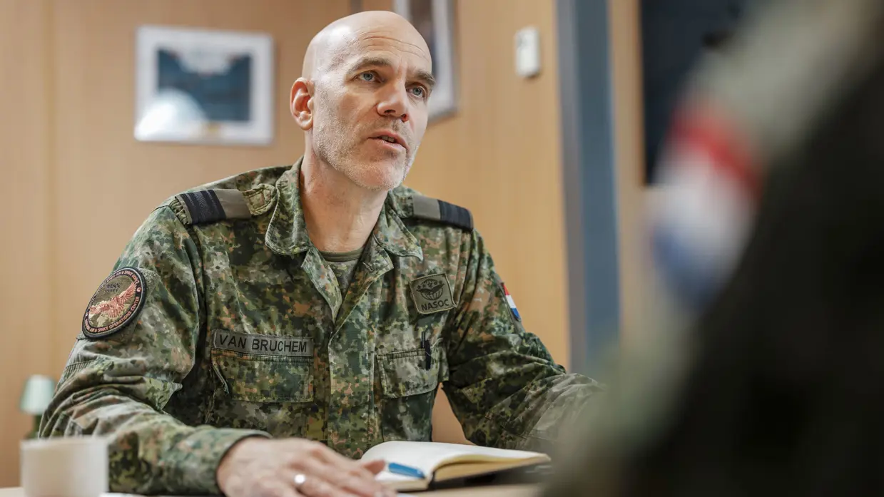 Commodore Jeroen van Bruchem zit, in militair uniform, aan een tafel en praat. Daarbij maakt hij gebruik van zijn handen.