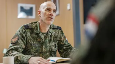 Commodore Jeroen van Bruchem zit, in militair uniform, aan een tafel en praat. Daarbij maakt hij gebruik van zijn handen.