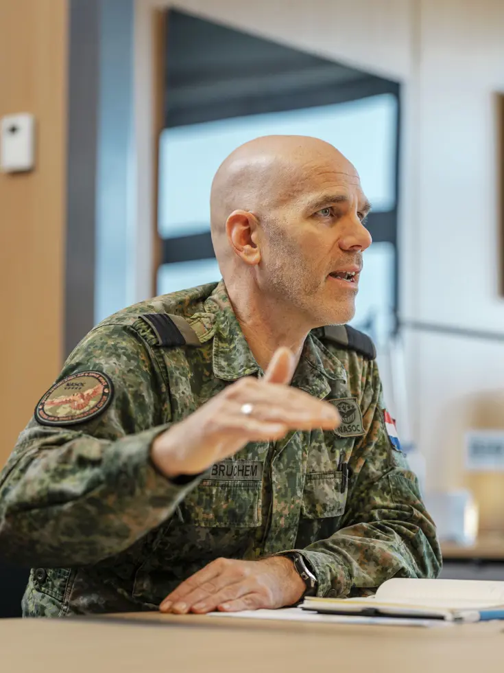 Commodore Jeroen van Bruchem zit, in militair uniform, aan een tafel en praat. Daarbij maakt hij gebruik van zijn handen.