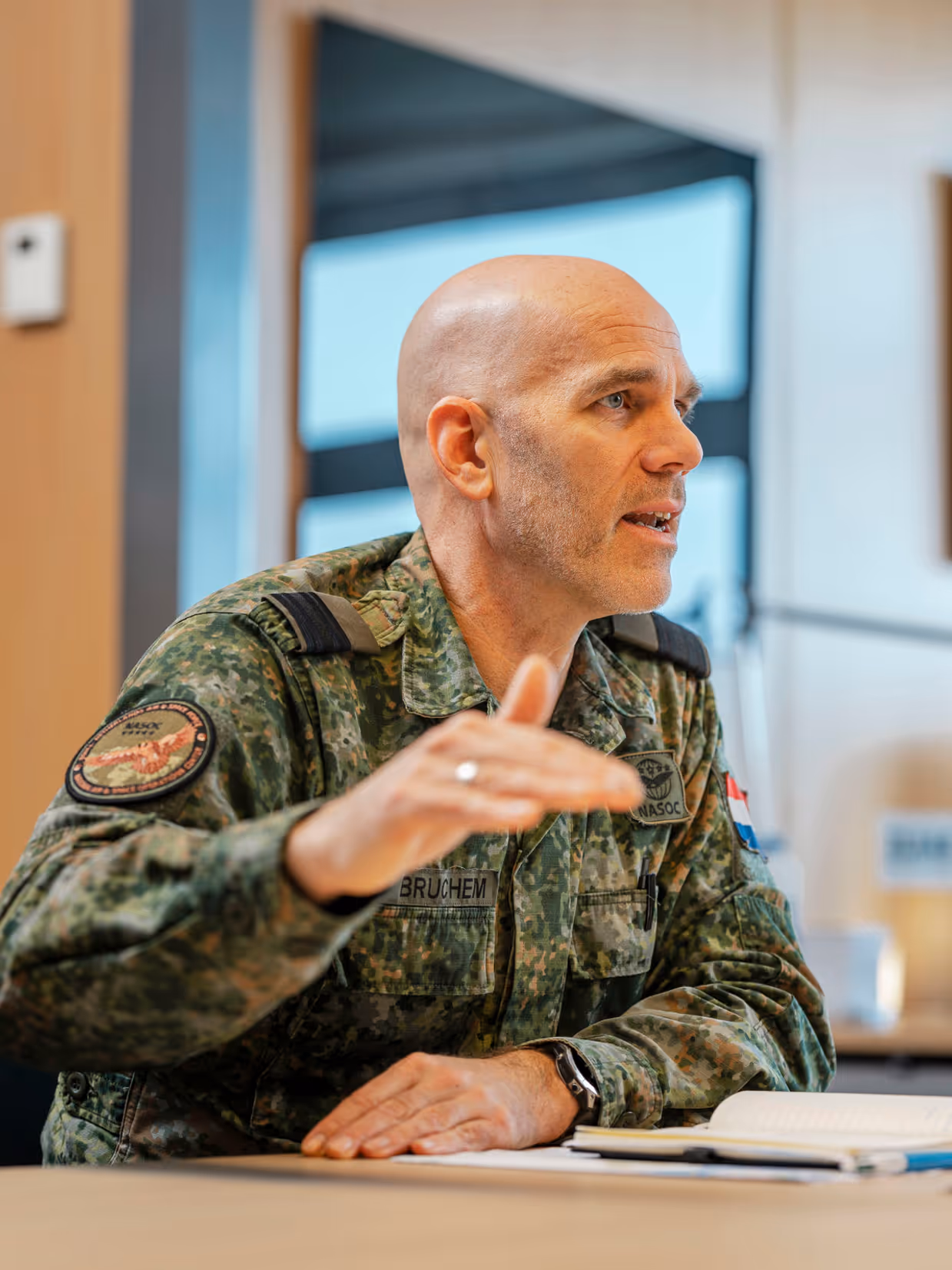 Commodore Jeroen van Bruchem zit, in militair uniform, aan een tafel en praat. Daarbij maakt hij gebruik van zijn handen.
