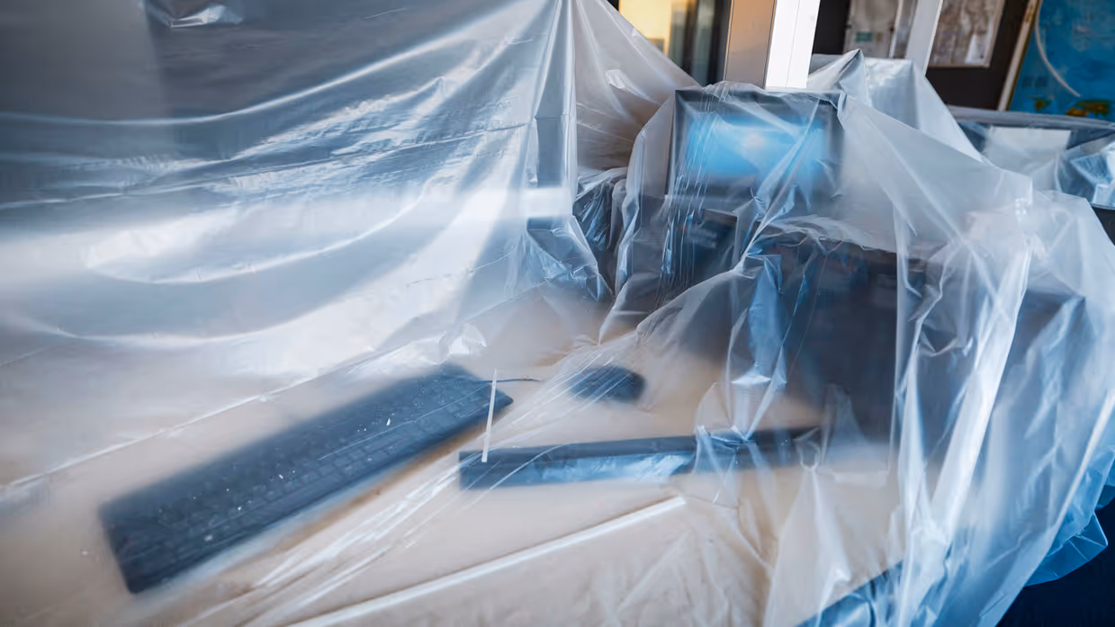 Vier foto’s van werkzaamheden. Naast een kantoorruimte met afgedekte bureaus, laptops en toetsenborden gaat het om een kabel die uit het plafond hangt. Tot slot het logo van de luchtmacht tegen een muur, daarnaast een afgedekt beeldscherm.