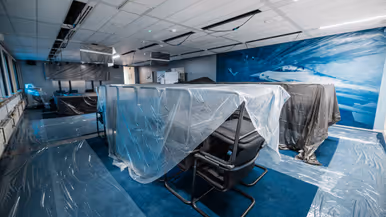 Vier foto’s van werkzaamheden. Naast een kantoorruimte met afgedekte bureaus, laptops en toetsenborden gaat het om een kabel die uit het plafond hangt. Tot slot het logo van de luchtmacht tegen een muur, daarnaast een afgedekt beeldscherm.