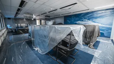 Vier foto’s van werkzaamheden. Naast een kantoorruimte met afgedekte bureaus, laptops en toetsenborden gaat het om een kabel die uit het plafond hangt. Tot slot het logo van de luchtmacht tegen een muur, daarnaast een afgedekt beeldscherm.