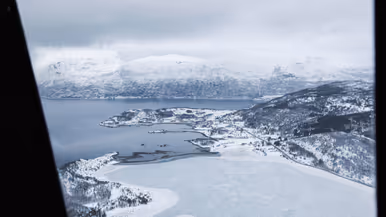 Een sneeuw- en ijsvlakte grenzend aan een fjord, gezien vanuit een helikopter.