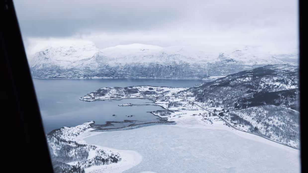 Een sneeuw- en ijsvlakte grenzend aan een fjord, gezien vanuit een helikopter.