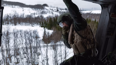 Loadmaster kijkt vanuit de open deur van een NH90 naar het besneeuwde landschap in Noorwegen tijdens oefening Cold Response.