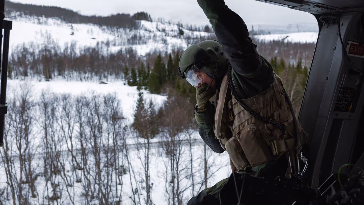Loadmaster kijkt vanuit de open deur van een NH90 naar het besneeuwde landschap in Noorwegen tijdens oefening Cold Response.