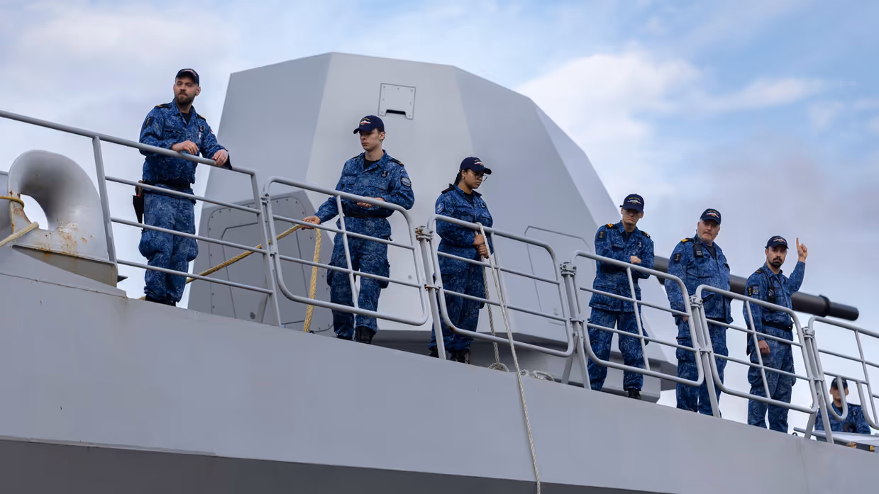 Links: Bemanningsleden bij de reling, met het scheepskanon op de achtergrond. Rechts: bemanning aan boord. Een van hen heeft een koptelefoon vast. 
