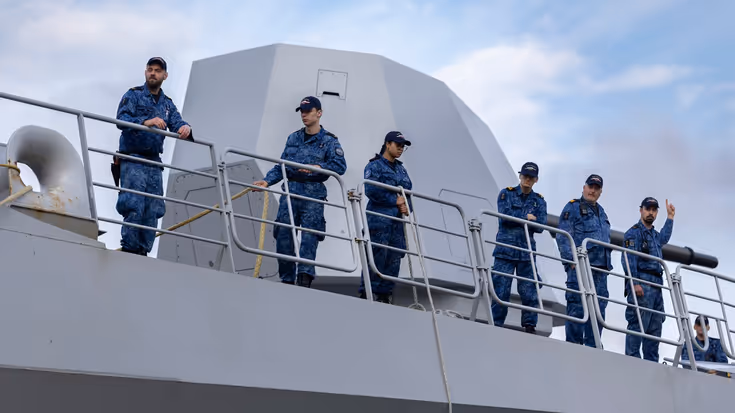 Bemanningsleden bij de reling, met het scheepskanon op de achtergrond. 
