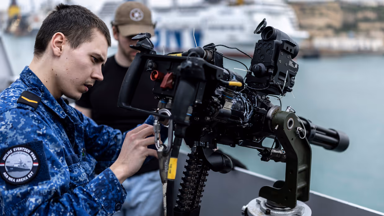 Marinepersoneel monteert een minigun op een reling. 