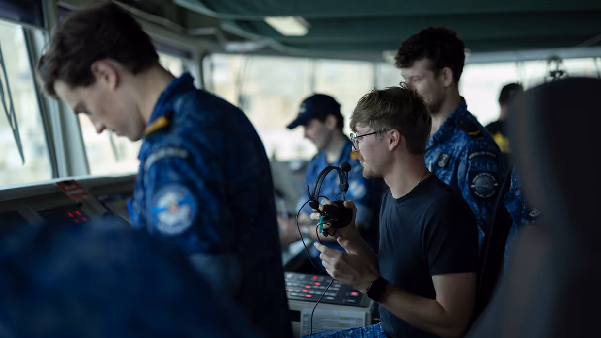 Links: Bemanningsleden bij de reling, met het scheepskanon op de achtergrond. Rechts: bemanning aan boord. Een van hen heeft een koptelefoon vast. 