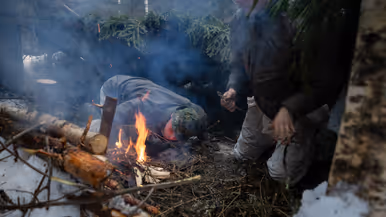 Onderkomen in de sneeuw  met op de voorgrond twee pax die een vuurtje aanblazen.