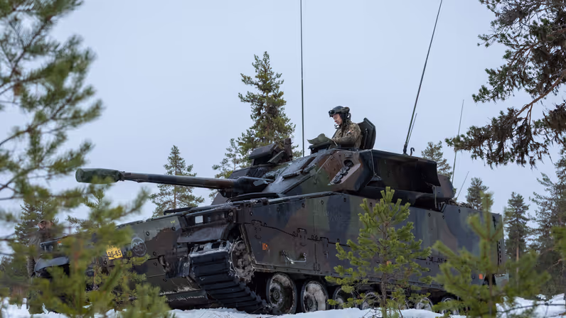 Een militair voertuig rijdt door een winters landschap.