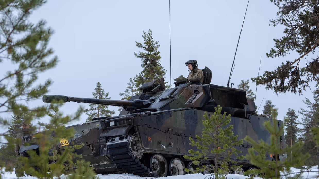 Een militair voertuig rijdt door een winters landschap.