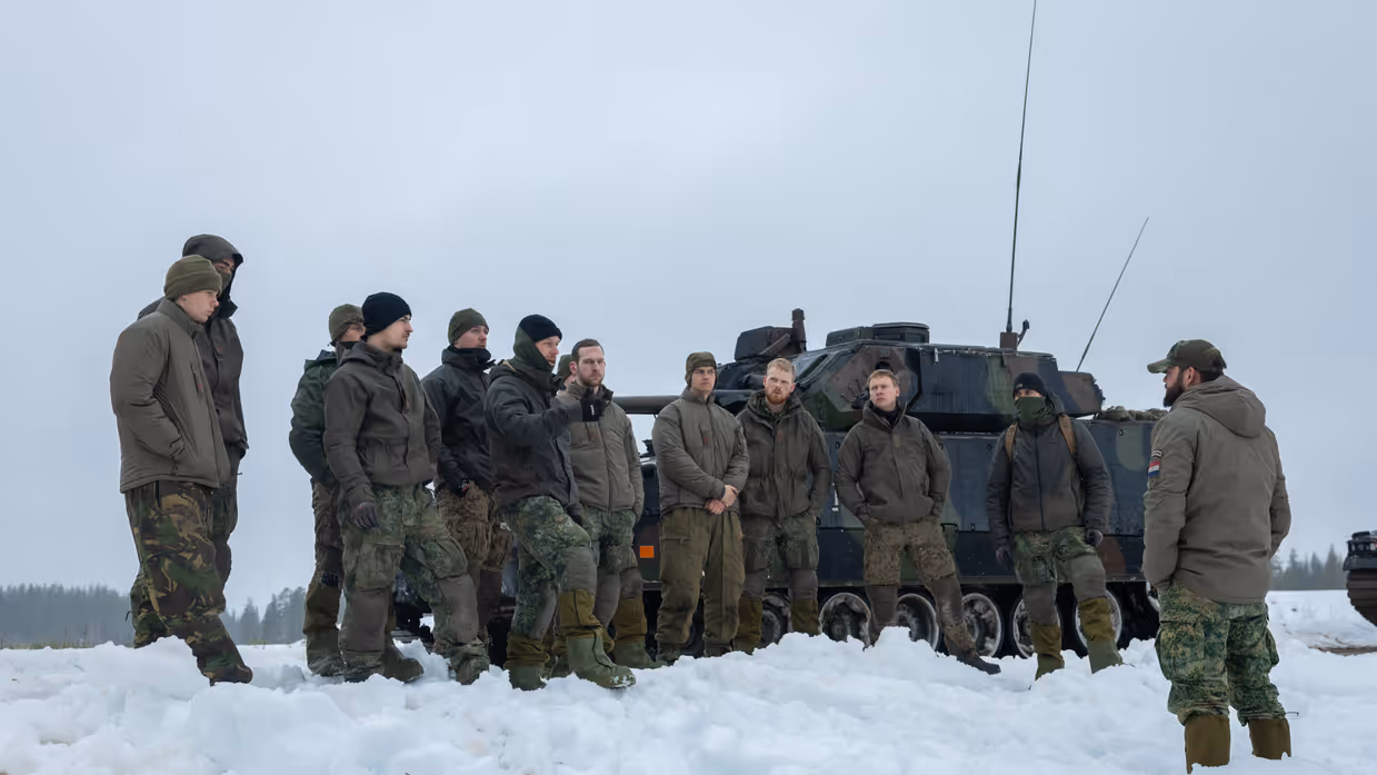 Manschappen krijgen in de sneeuw een evaluatie over de oefening, met op de achtergrond een CV90.