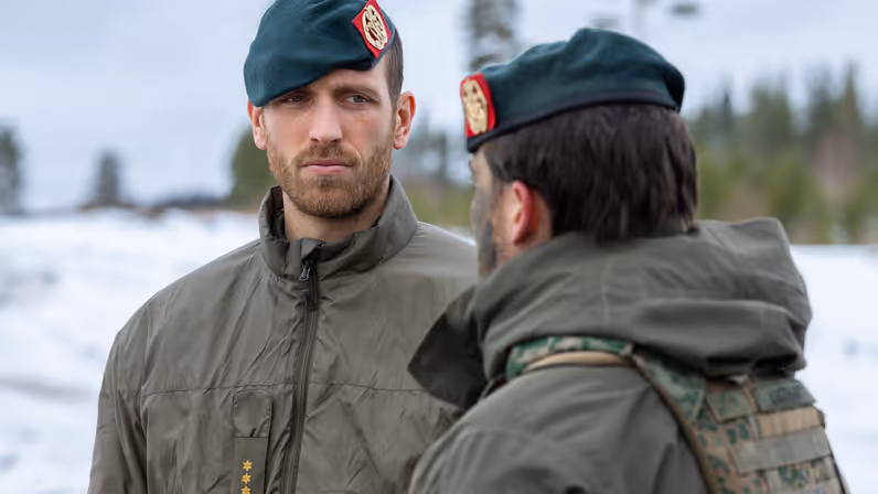 Kapitein Niels Wijnen in gesprek met een collega en op de achtergrond een winters landschap. 