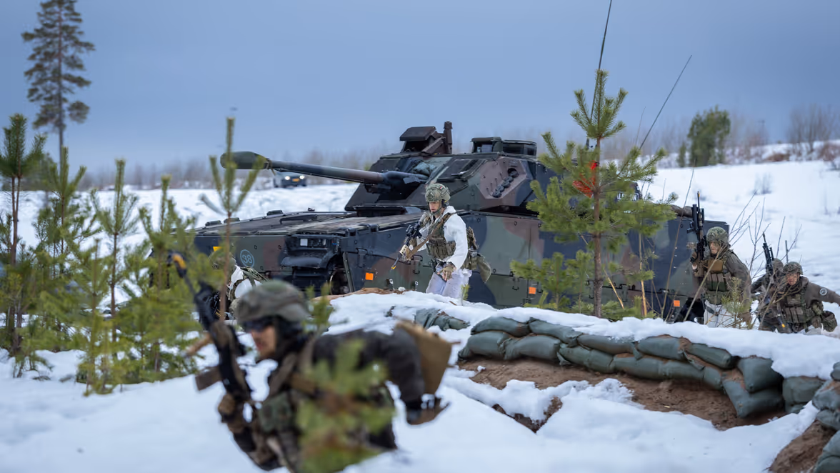 Een CV90 in een winters landschap brengt manschappen naar de rand van een loopgraaf.