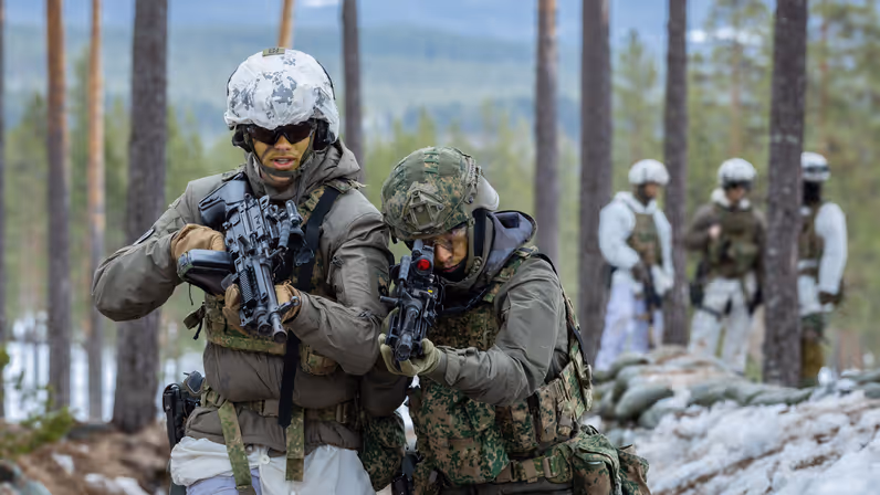 Twee oefenende militairen in de loopgraven, met gevechtsgeweren in de aanslag lopen ze richting de camera.