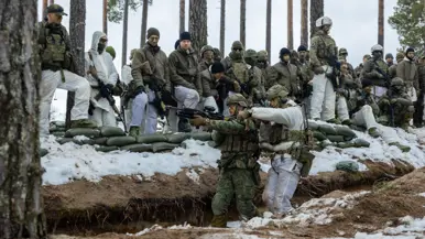 In het bos in winterse omstandigheden geven twee militairen aan collega’ s een demonstratie over verplaatsingen in een loopgraaf.