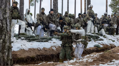 In het bos in winterse omstandigheden geven twee militairen aan collega’ s een demonstratie over verplaatsingen in een loopgraaf.