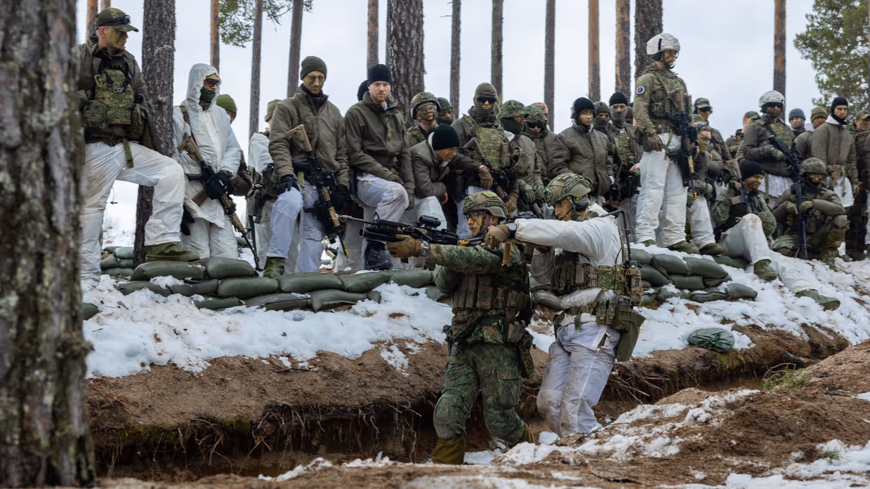 In het bos in winterse omstandigheden geven twee militairen aan collega’ s een demonstratie over verplaatsingen in een loopgraaf.
