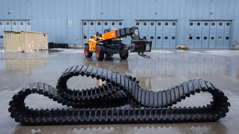 Een grote rubberen band ligt op de grond, erachter staat een kraanwagen. 